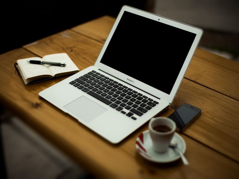 laptop on brown table, notepad and cup of coffee